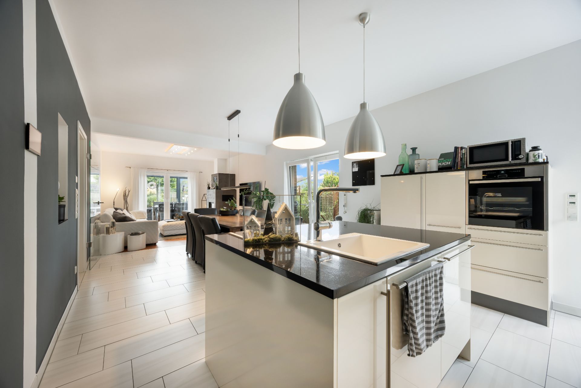 Moderne offene Küche mit Kochinsel, Essbereich und Zugang zum Wohnzimmer, helle Fenster im Hintergrund.