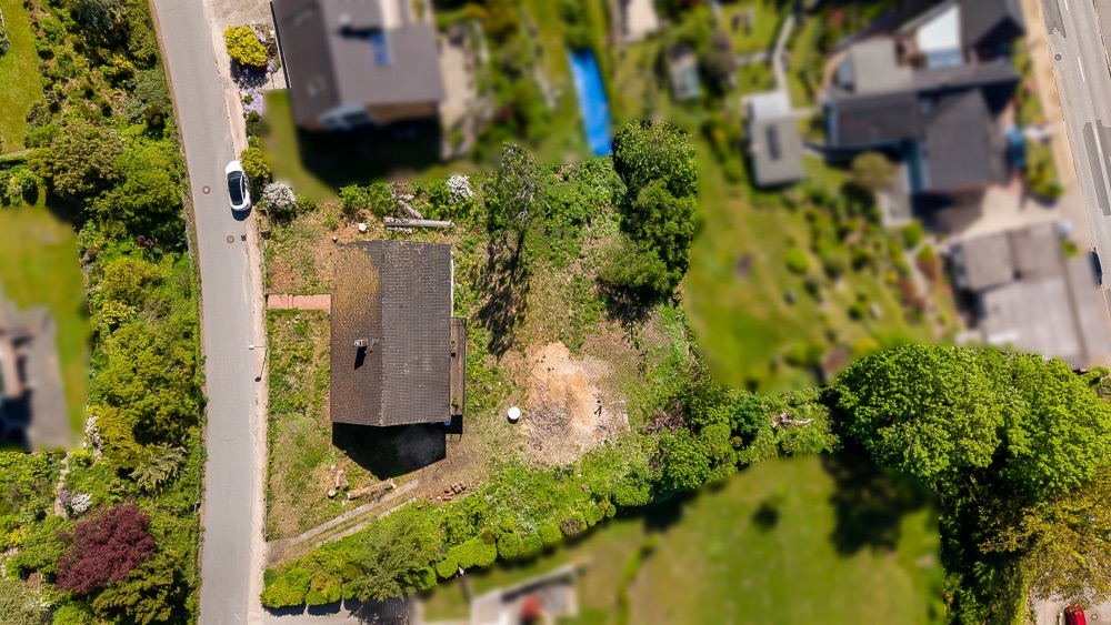 Luftaufnahme eines Grundstücks mit einem Haus, umgeben von Bäumen und einer Straße.
