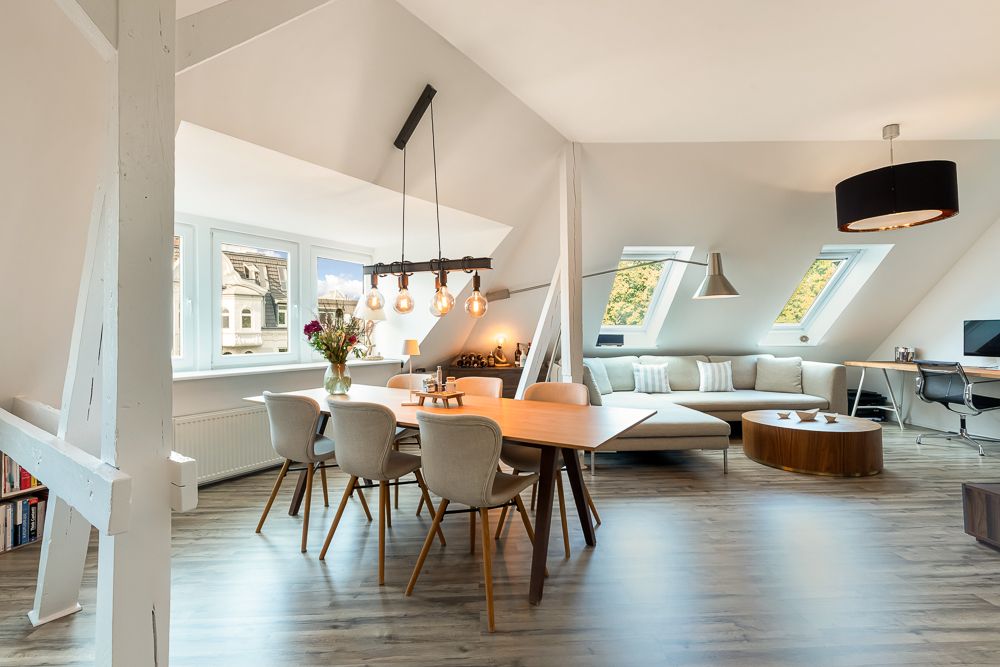 Helles Wohnzimmer mit Esstisch, Stühlen, Sofa und Schreibtisch unter Dachschrägen.