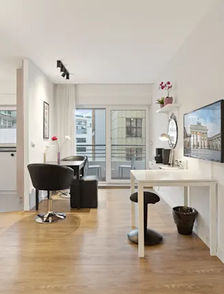 Helles Apartment mit Holzboden, Schreibtisch, Fernseher, Bett und kleinem Balkon.