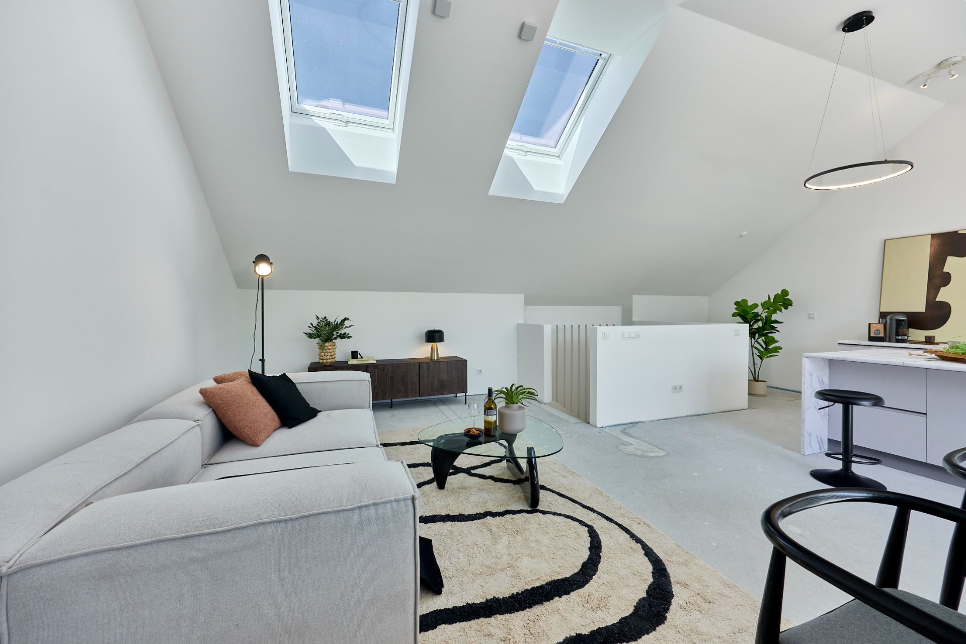 Helles Wohnzimmer mit Dachfenstern, Sofa, Teppich und kleiner Sitzecke in modernem Stil.