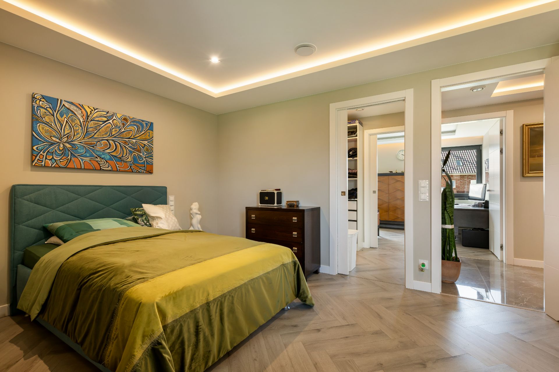 Modernes Schlafzimmer mit grünem Bett, Kommode und farbigem Wandbild, Türen führen in andere Räume.