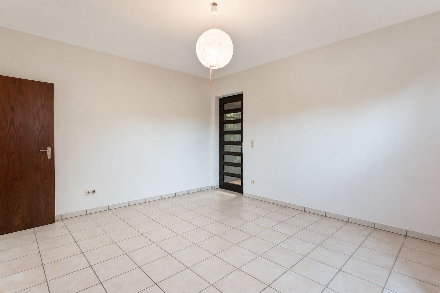Leerer Raum mit weißen Fliesen, Holztür, Glastür und Lampe an der Decke.