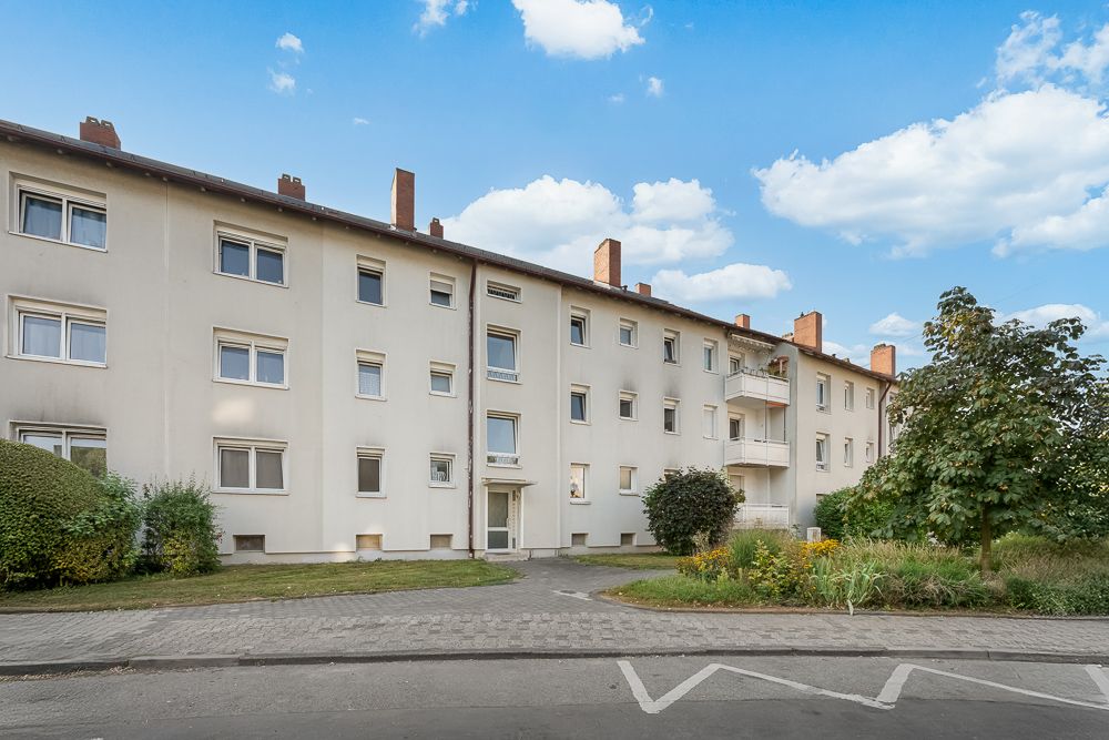 Mehrfamilienhaus mit drei Etagen, großem Eingang und umliegenden Bäumen.