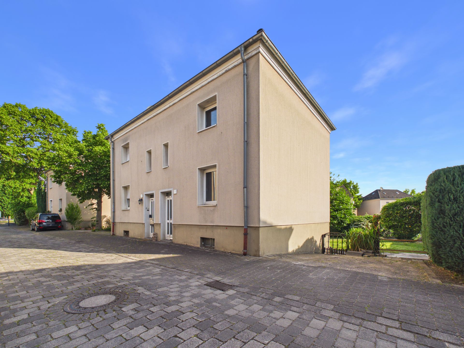 Zweistöckiges Wohnhaus mit beigem Putz und mehreren Fenstern, davor gepflasterte Straße.
