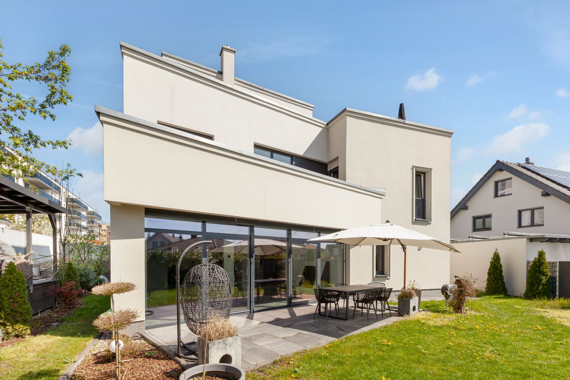 Modernes Wohnhaus mit Terrasse, Gartenmöbeln und Sonnenschirm im Garten.