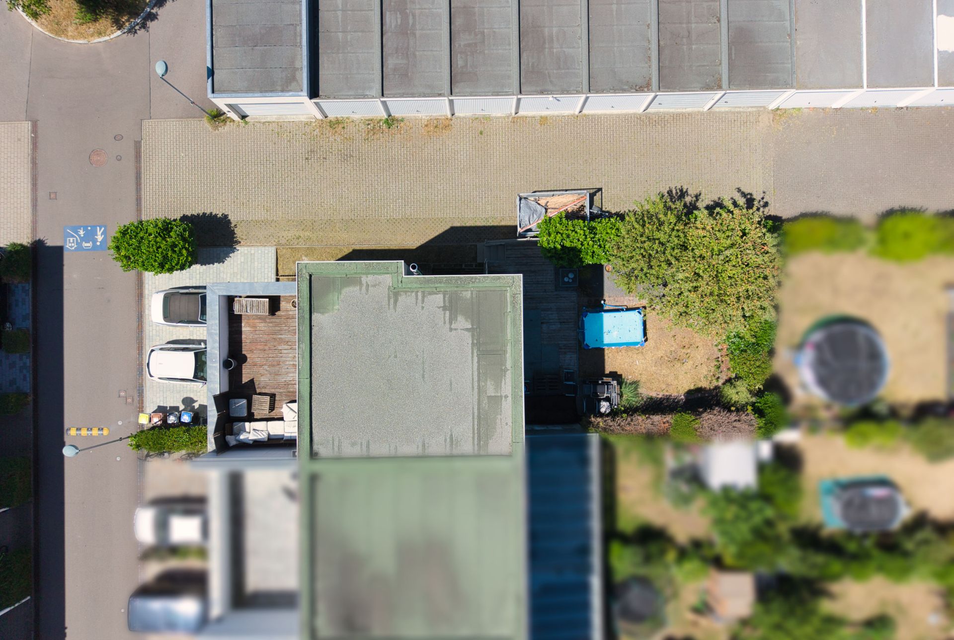 Draufsicht auf ein Wohnhaus mit Terrasse, zwei geparkten Autos und Garten mit kleinem Pool.