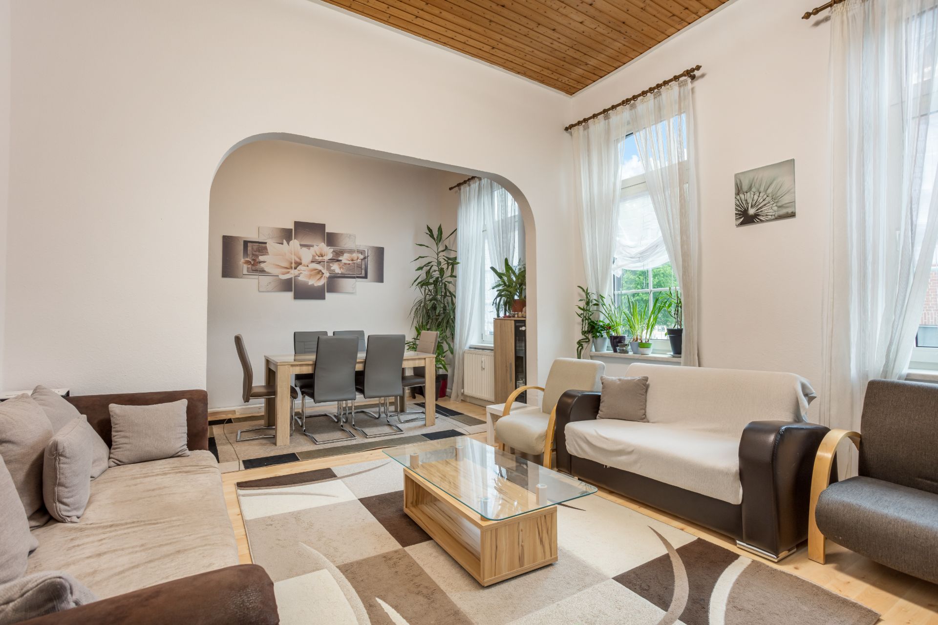 Helles Wohnzimmer mit Sofas, Couchtisch, Teppich und Durchgang zum Esszimmer mit Esstisch und Stühlen.