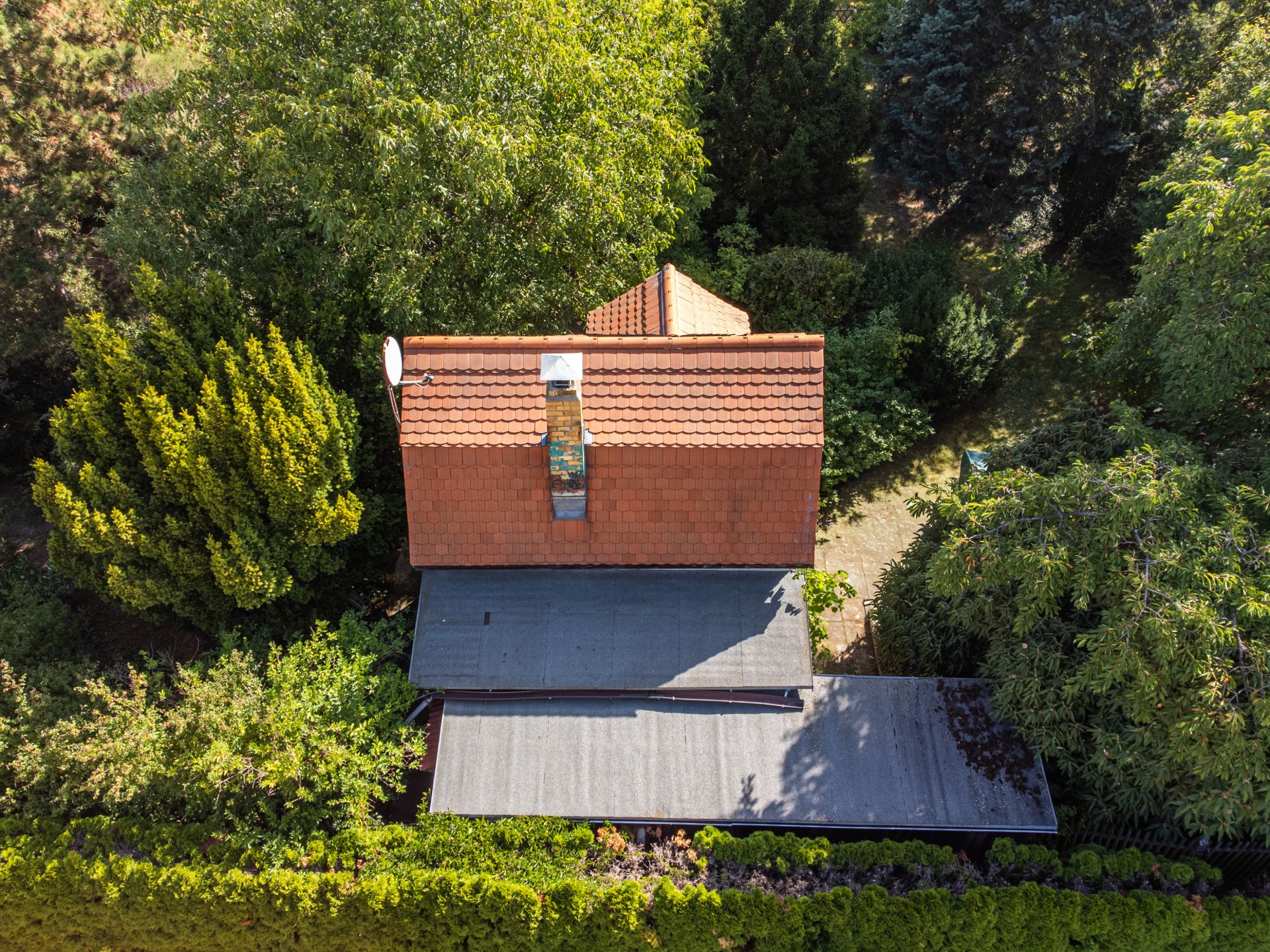 Luftaufnahme eines Hauses mit rotem Ziegeldach, umgeben von dichtem grünen Garten.