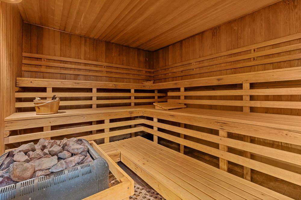 Innenraum einer holzverkleideten Sauna mit Bänken und einem Saunaofen mit Steinen.