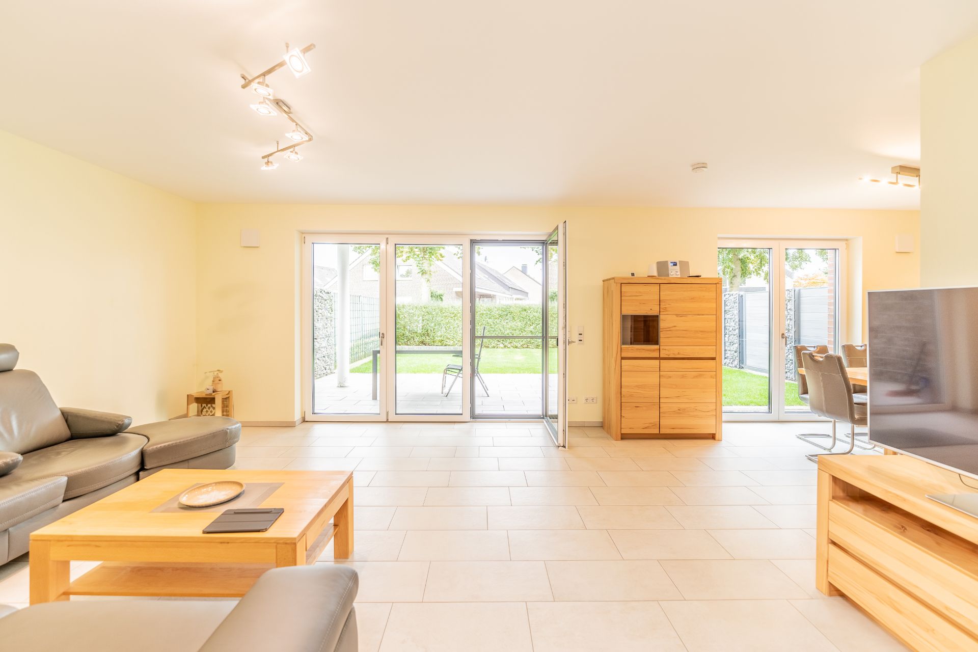 Helles Wohnzimmer mit grauen Sofas, Holzmöbeln und großen Fenstern zum Garten.