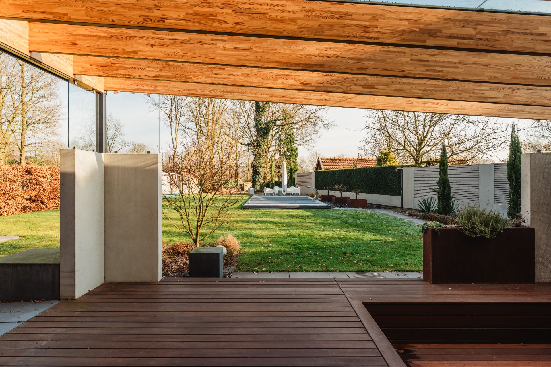 Überdachte Holzterrasse mit Blick auf einen gepflegten Garten und modernen Sitzbereich im Freien.