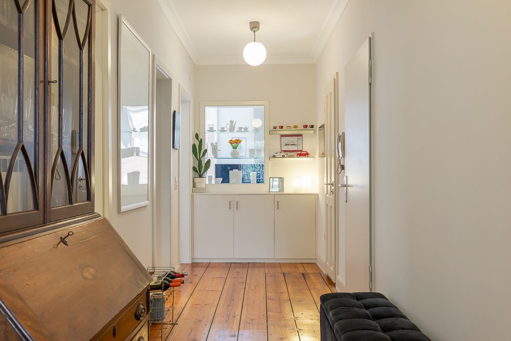 Heller Flur mit Holzboden, weißen Wänden und Sideboard, Spiegel und Dekoration.