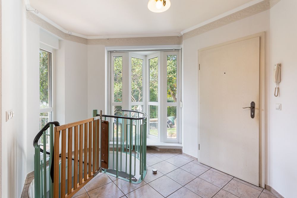 Heller Flur mit großer Fensterfront, Treppengeländer und Holztür.