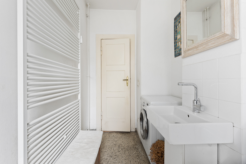 Helles Badezimmer mit Waschbecken, Spiegel, Waschmaschine und weißem Heizkörper.