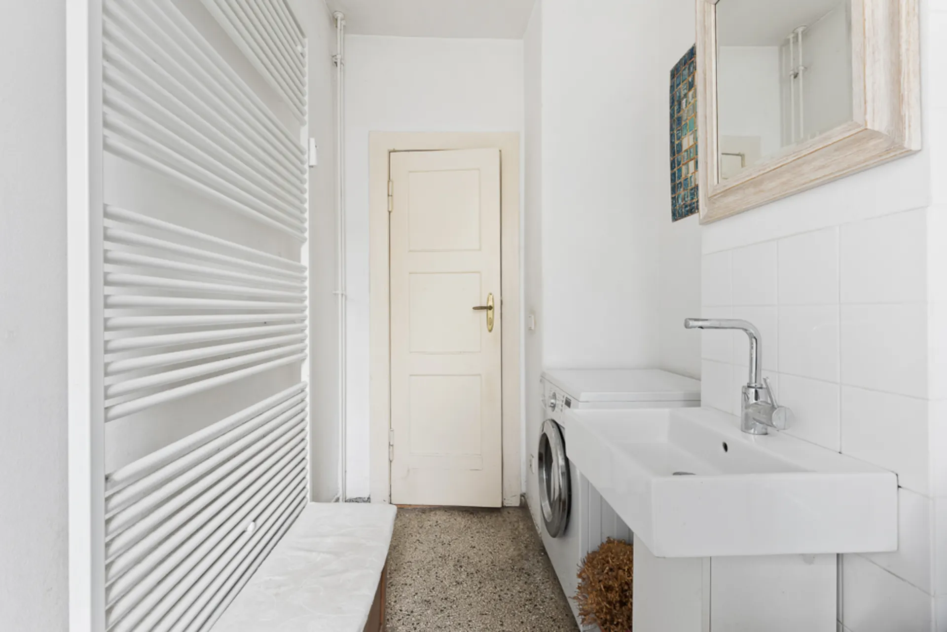 Helles Badezimmer mit Waschbecken, Spiegel, Waschmaschine und weißem Heizkörper.