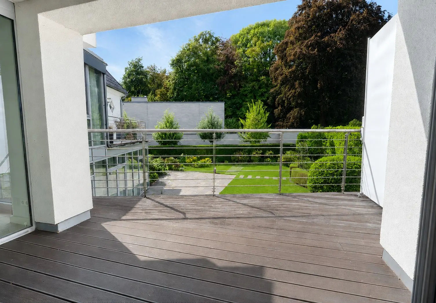 Moderne Terrasse mit Holzboden und Blick auf gepflegten Garten mit Rasen und Bäumen.