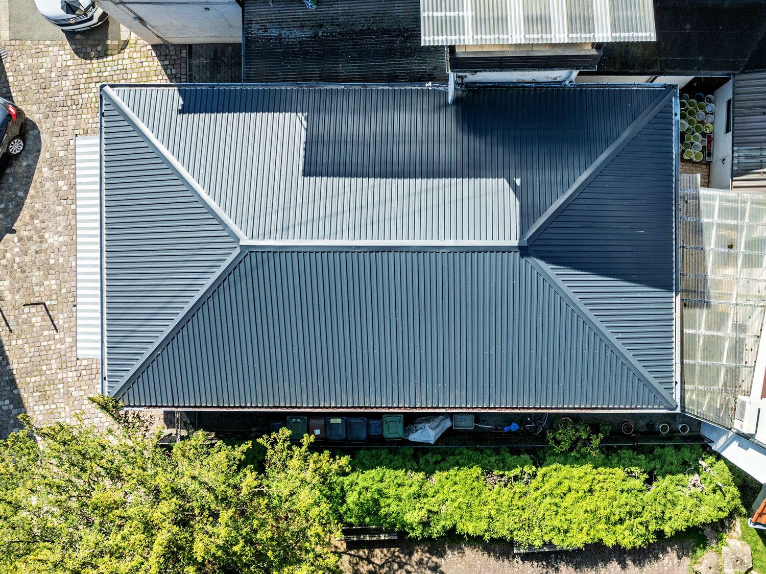 Draufsicht auf ein Haus mit dunkelgrauem Metalldach und umliegendem Garten.