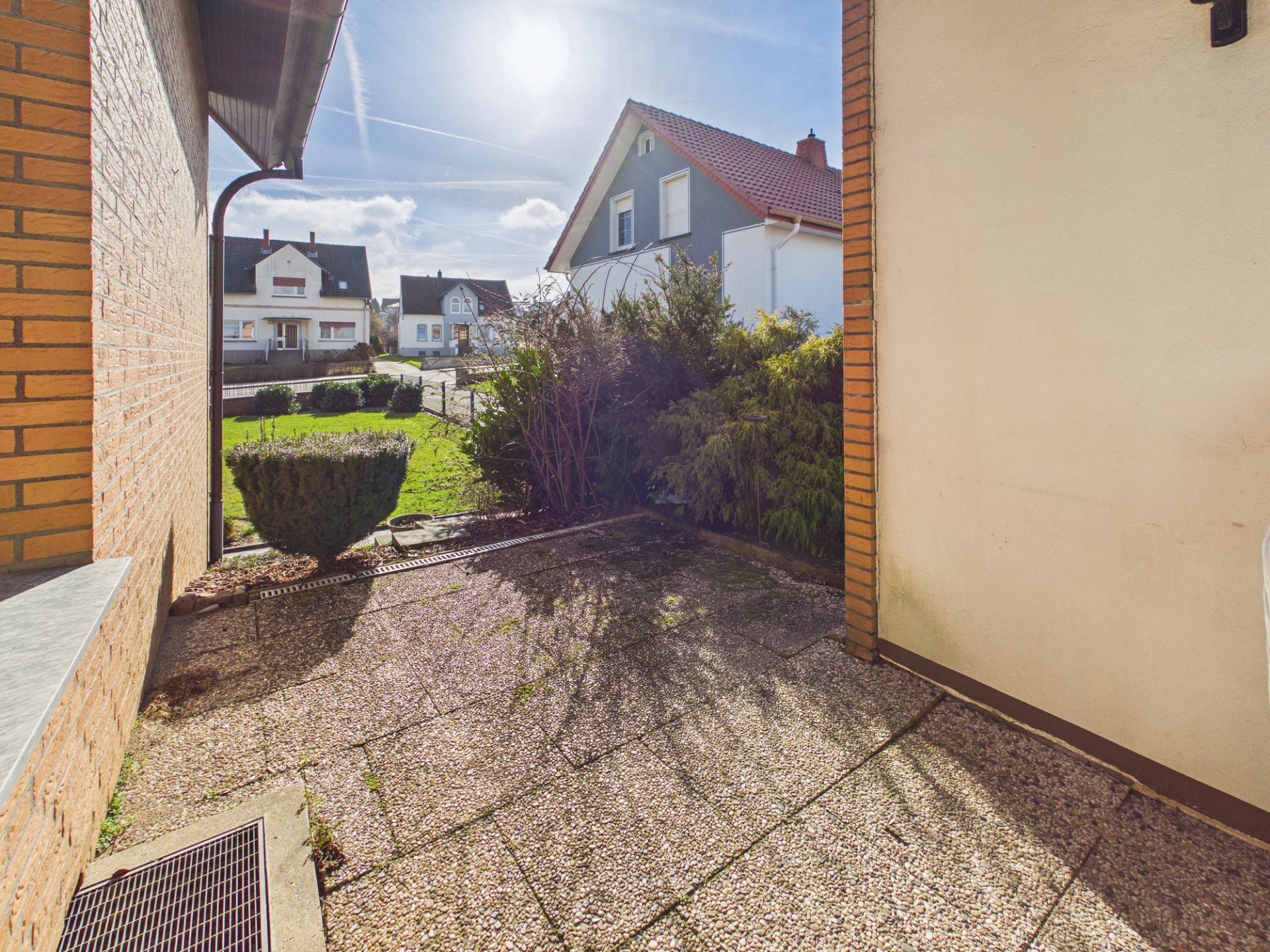 Gepflasterte Terrasse mit Blick auf einen Garten und Nachbarhäuser bei Sonnenschein.