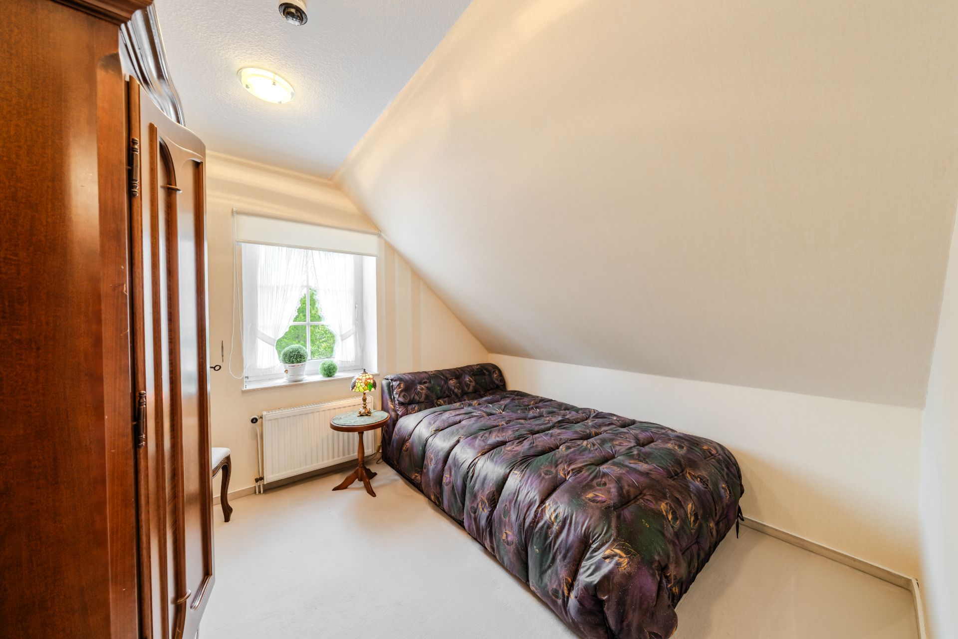 Kleines Schlafzimmer mit Dachschräge, Einzelbett, Holzschrank und Fenster mit Tageslicht.