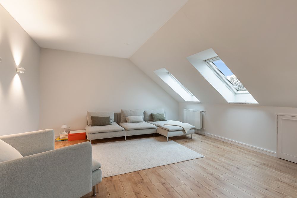 Helle Wohnzimmerecke mit Sofa, Sessel, Teppich und Dachfenstern auf Holzfußboden.