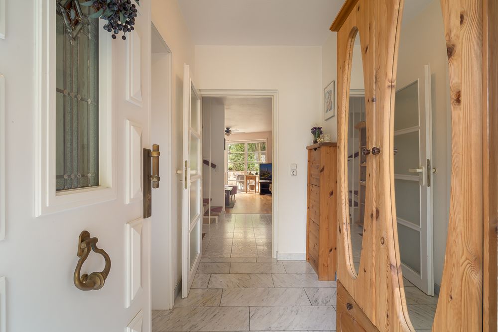 Heller Flur mit Holzmöbeln und Blick in ein Wohnzimmer mit großen Fenstern.