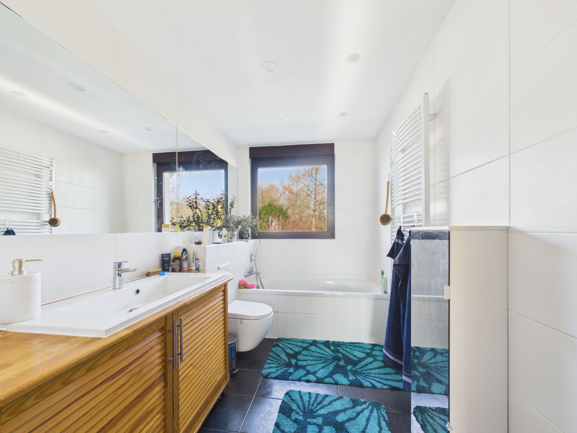 Modernes Badezimmer mit Badewanne, Doppelwaschbecken, großem Spiegel und zwei Fenstern.