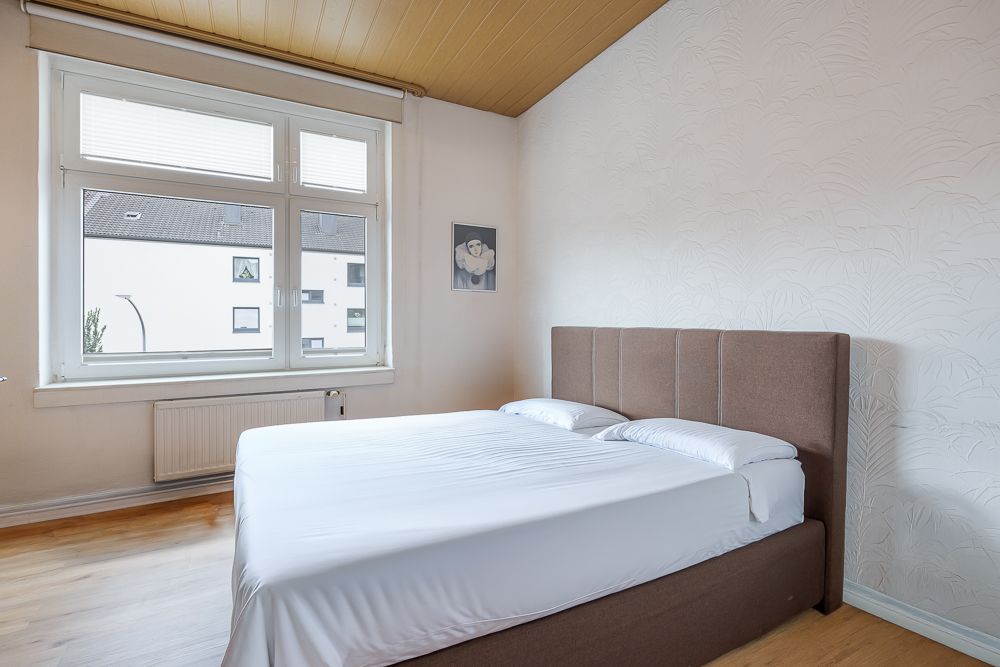 Schlafzimmer mit Doppelbett, großem Fenster und hellem Holzboden.