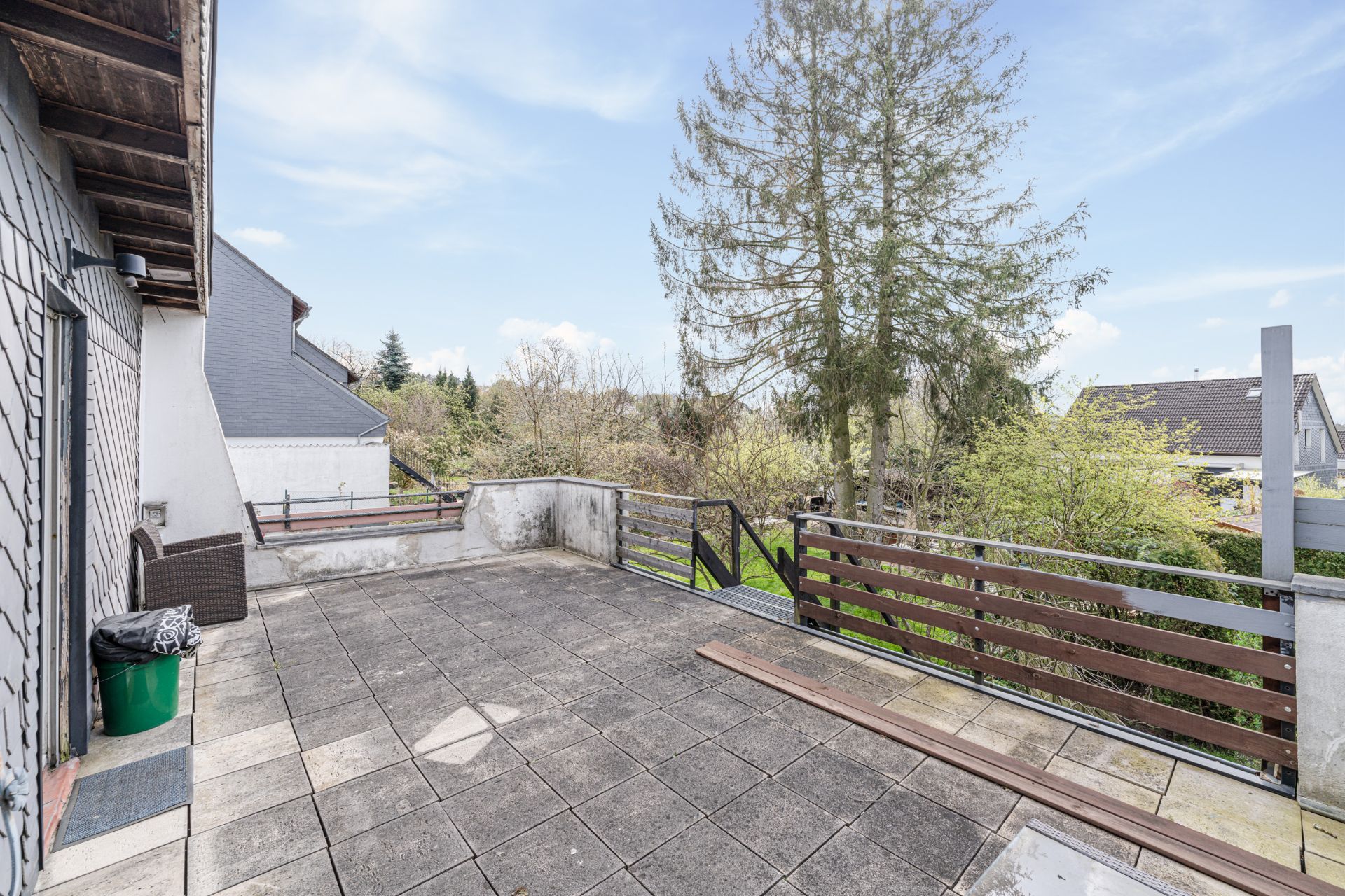 Große Terrasse mit Fliesenboden, Holzgeländer und Blick auf Bäume und Nachbarhäuser.