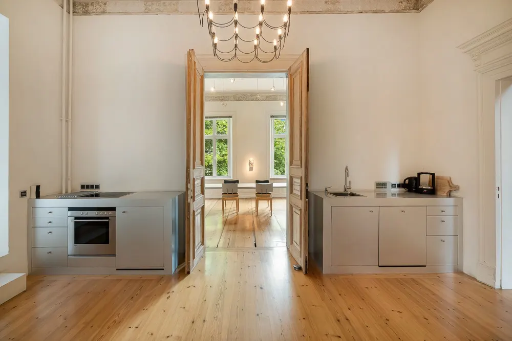 Moderne Küche mit Holzboden, offenem Durchgang und Blick auf einen hellen Wohnraum mit Fenstern.