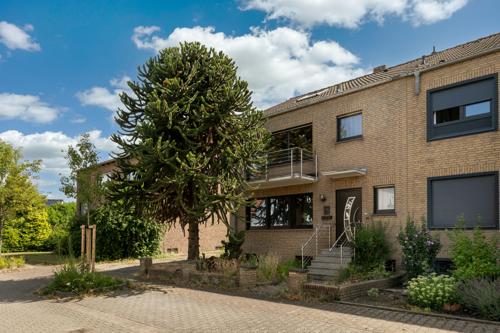 Zweistöckiges Wohnhaus mit großem Baum im Vorgarten und kleiner Treppe zum Eingang.