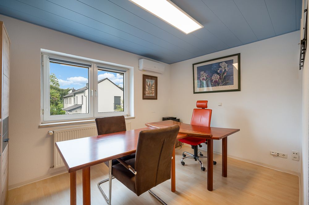 Helles Arbeitszimmer mit zwei Tischen, drei Stühlen und Bildern an der Wand.