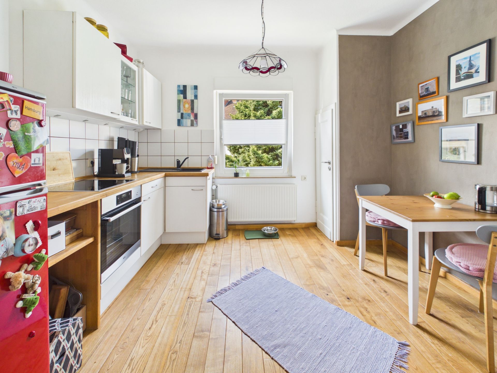 Helle Küche mit Holzboden, Esstisch, roten Kühlschrank und Fenster mit Blick ins Grüne.