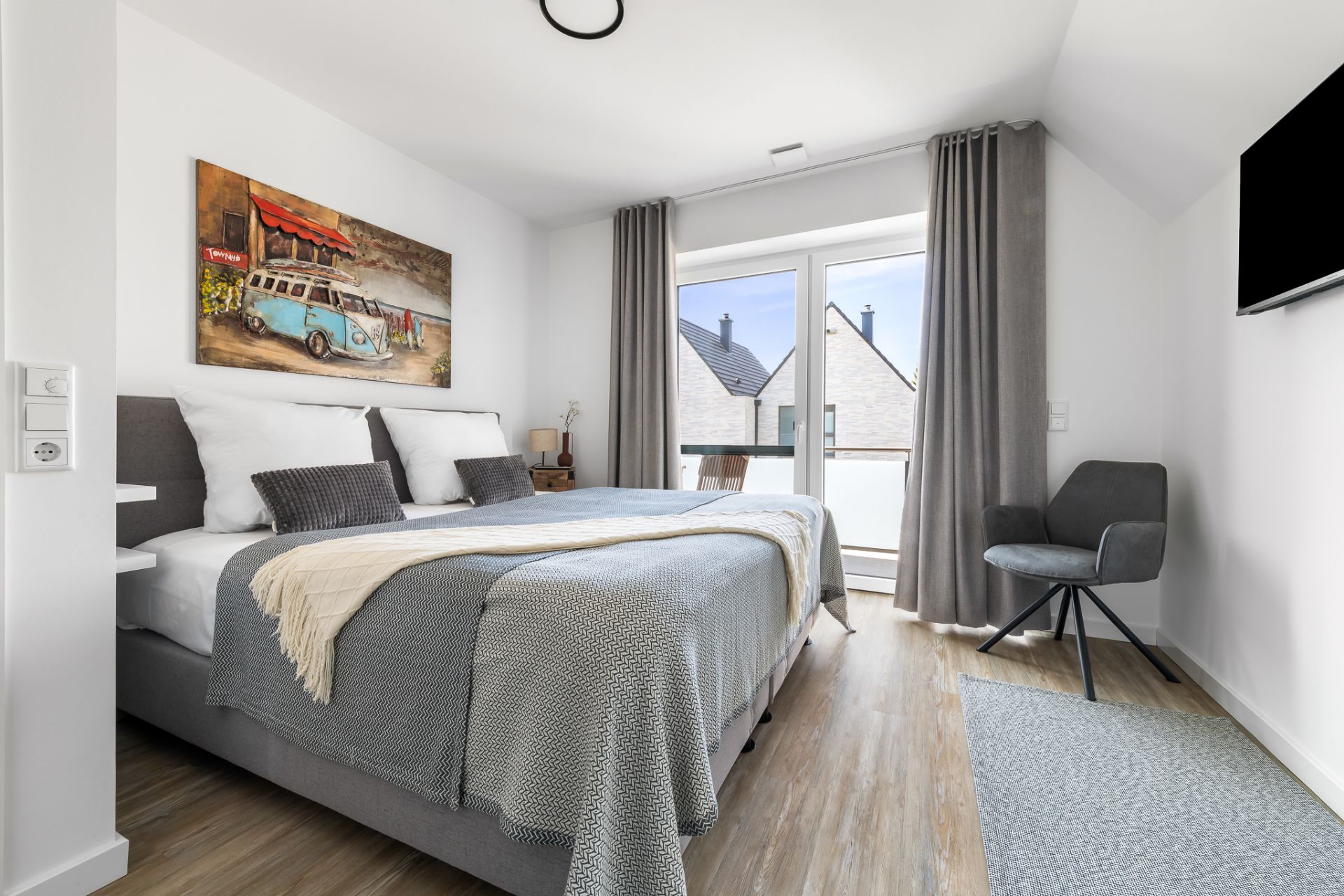 Modernes Schlafzimmer mit Doppelbett, Bild an der Wand, Sessel und Zugang zum Balkon.