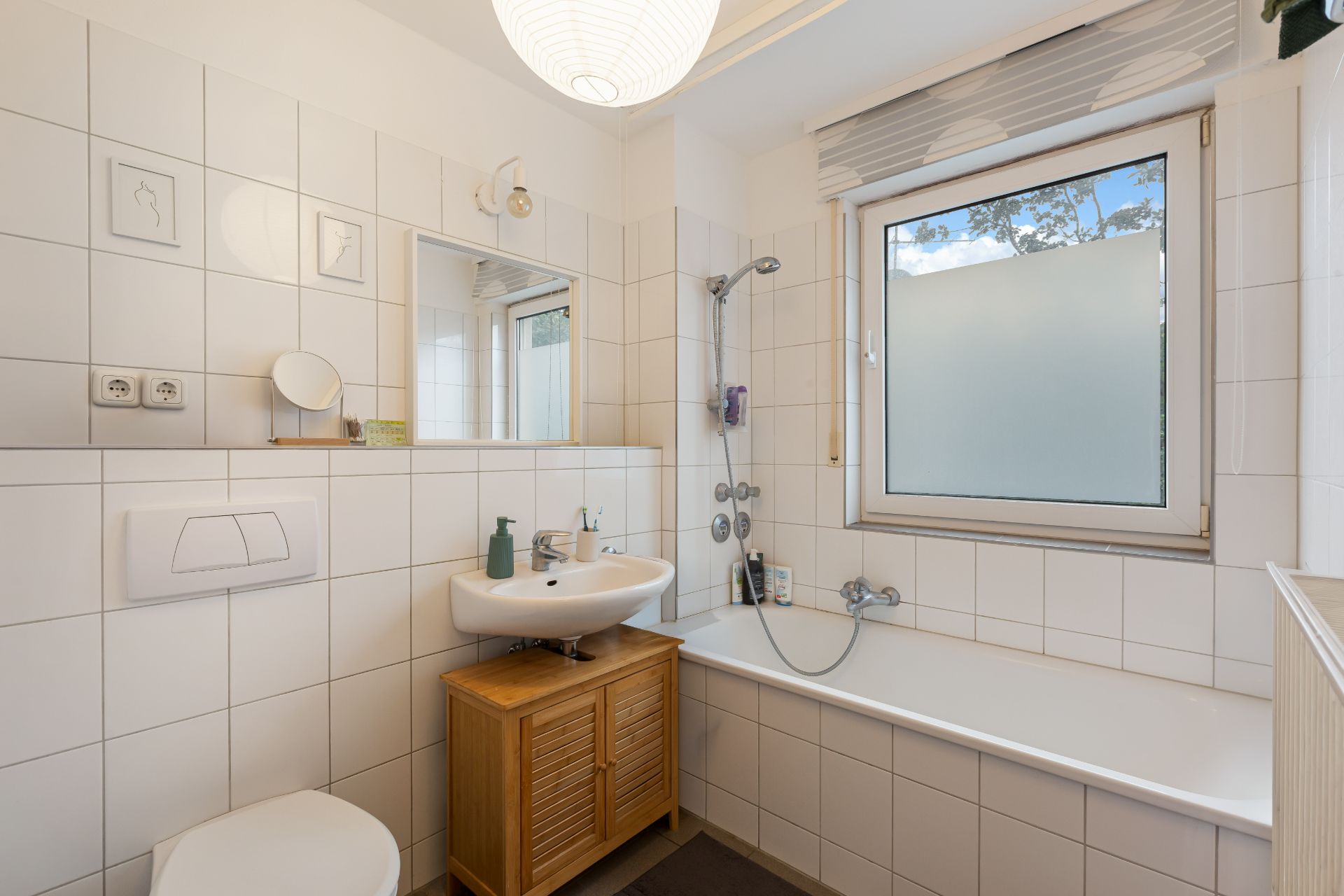 Helles Badezimmer mit Badewanne, Waschbecken, Spiegel und Fenster.