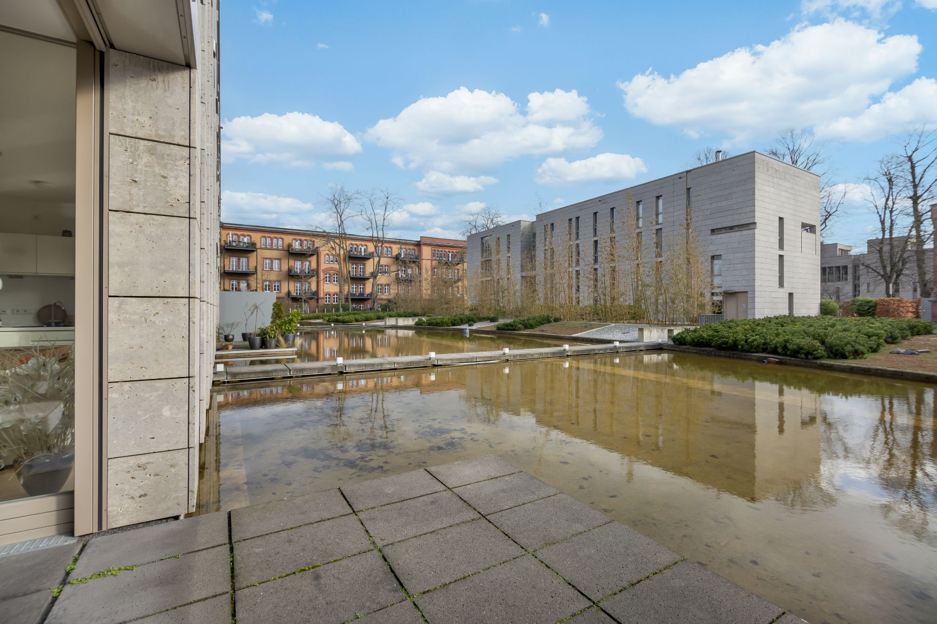 Moderner Innenhof mit Wasserbecken, Gehweg und Wohngebäuden im Hintergrund.