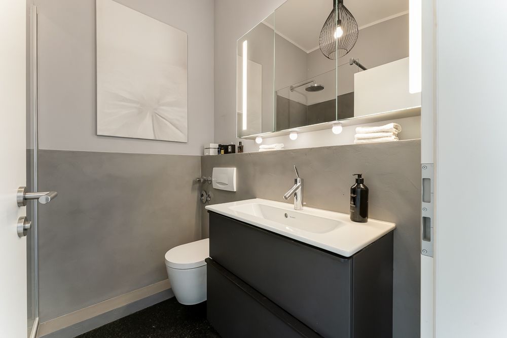 Modernes Bad mit Waschbecken, Spiegel, Hängeschrank, WC und Handtüchern.