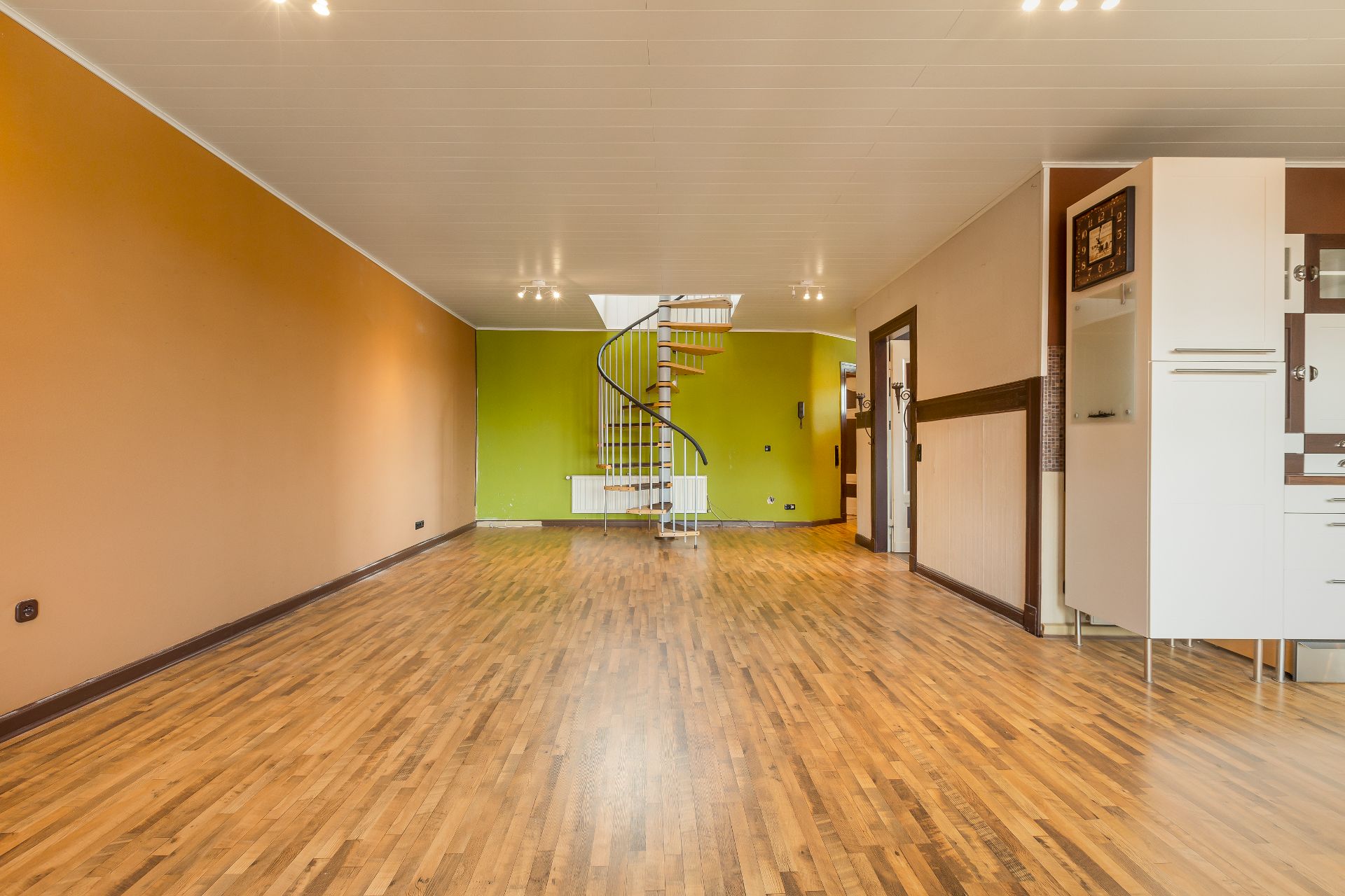 Heller Raum mit Holzfußboden, Wendeltreppe und offener Küche.