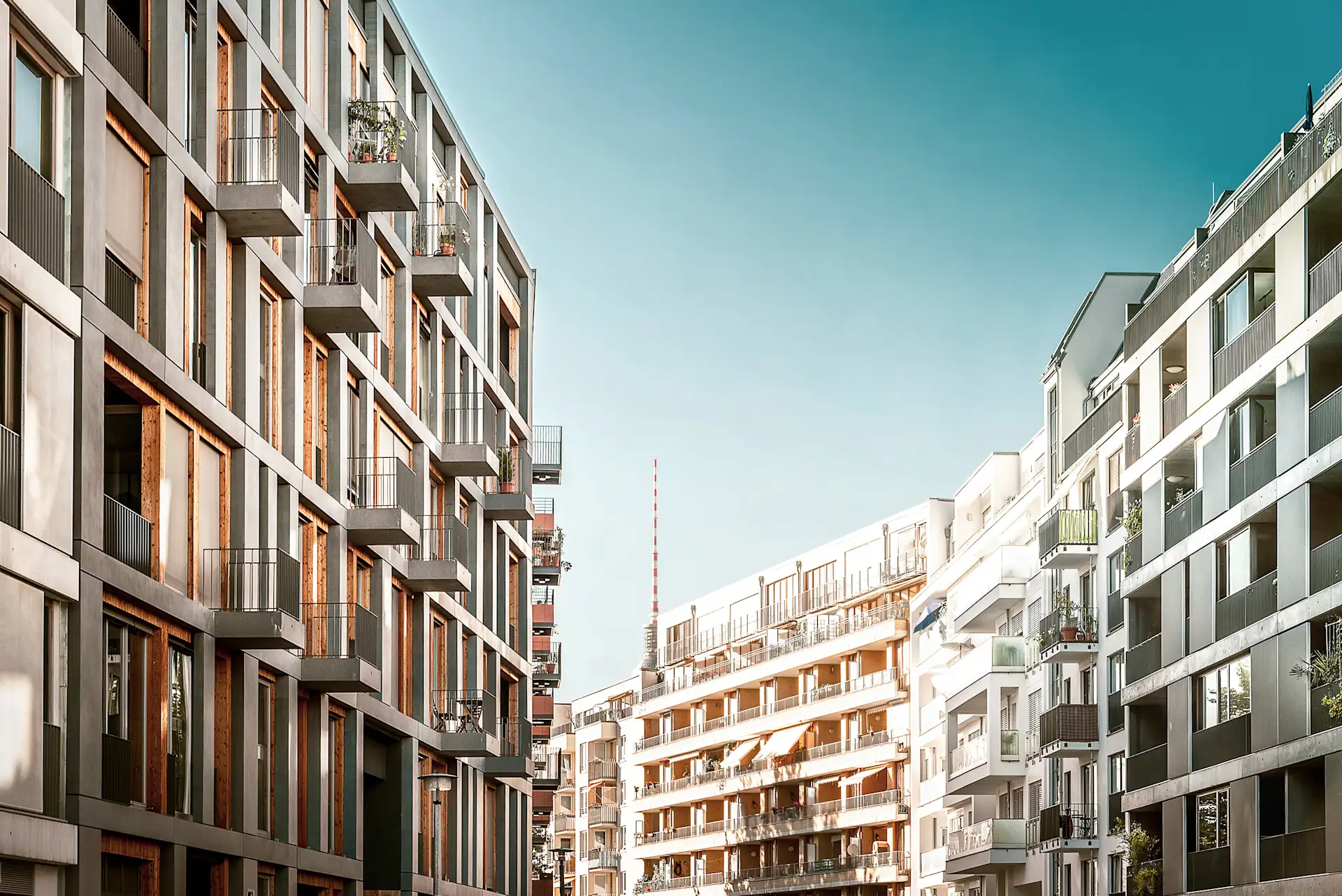 Moderne Wohngebäude mit Balkonen an einer Straße bei klarem Himmel.