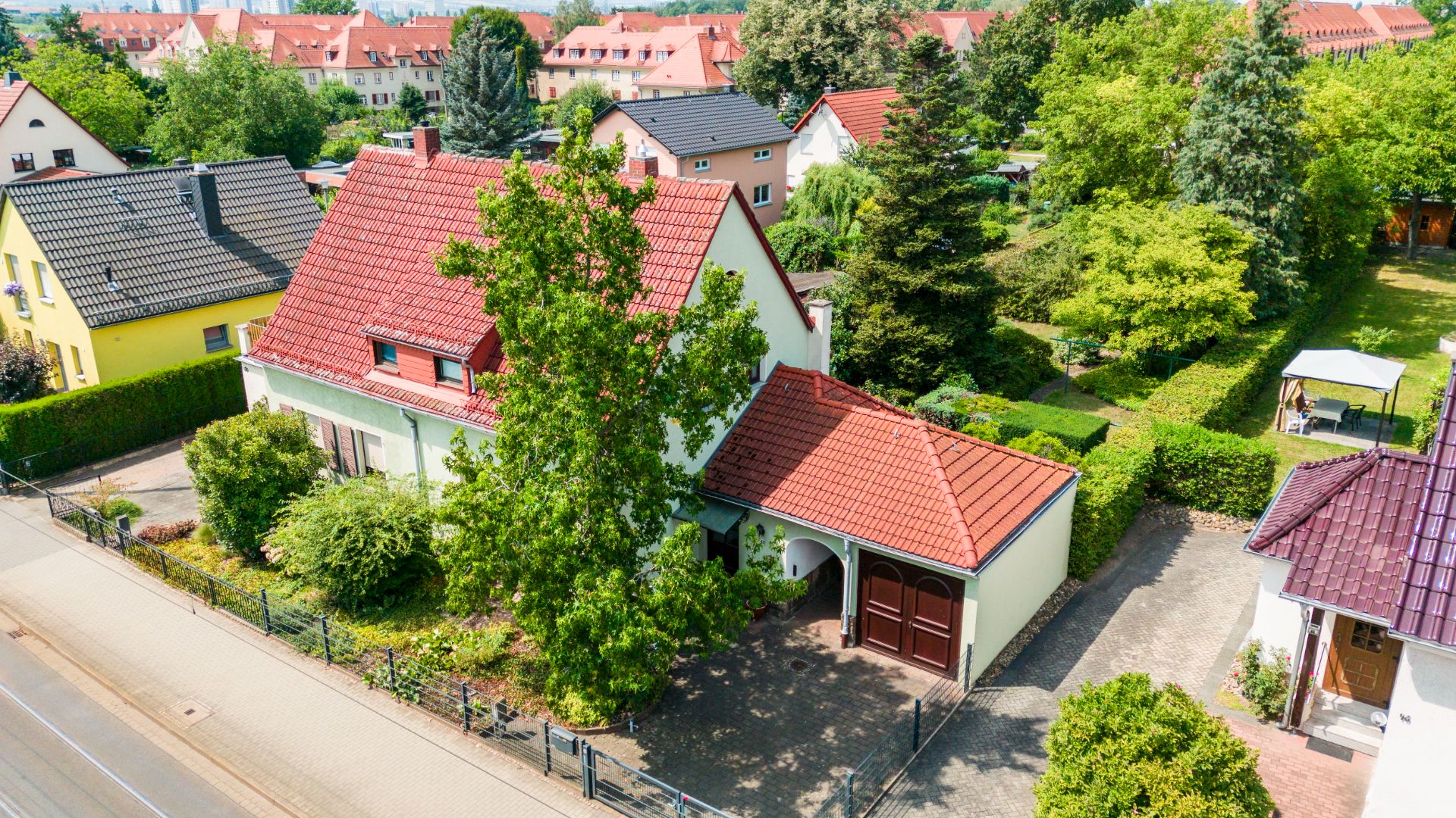 Einfamilienhaus mit rotem Dach, Garage, Garten und Bäumen, aus der Vogelperspektive.