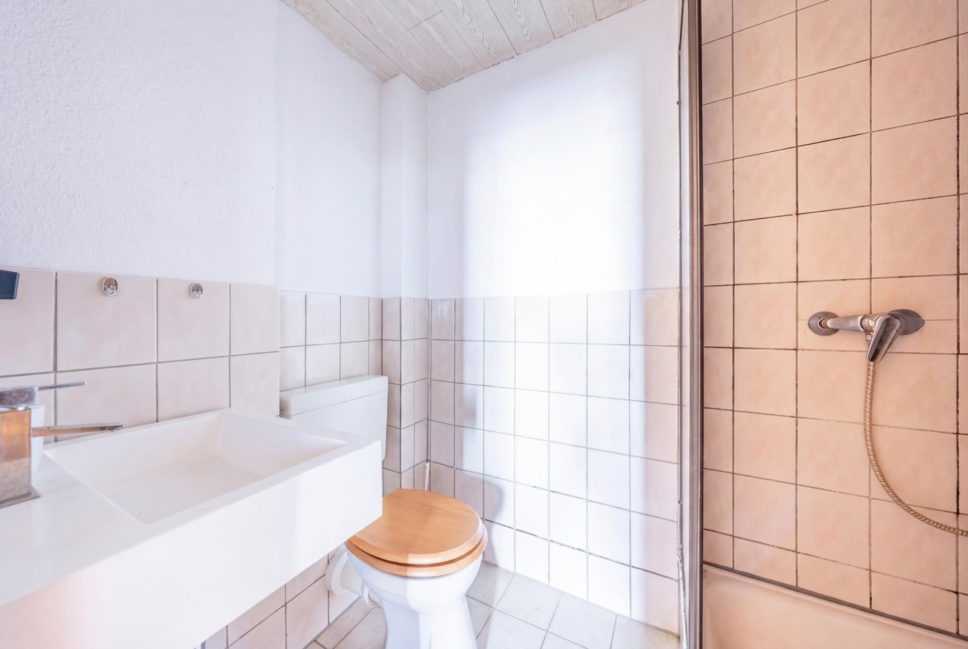 Helles Bad mit Waschbecken, WC mit Holzsitz und Dusche mit Handbrause.