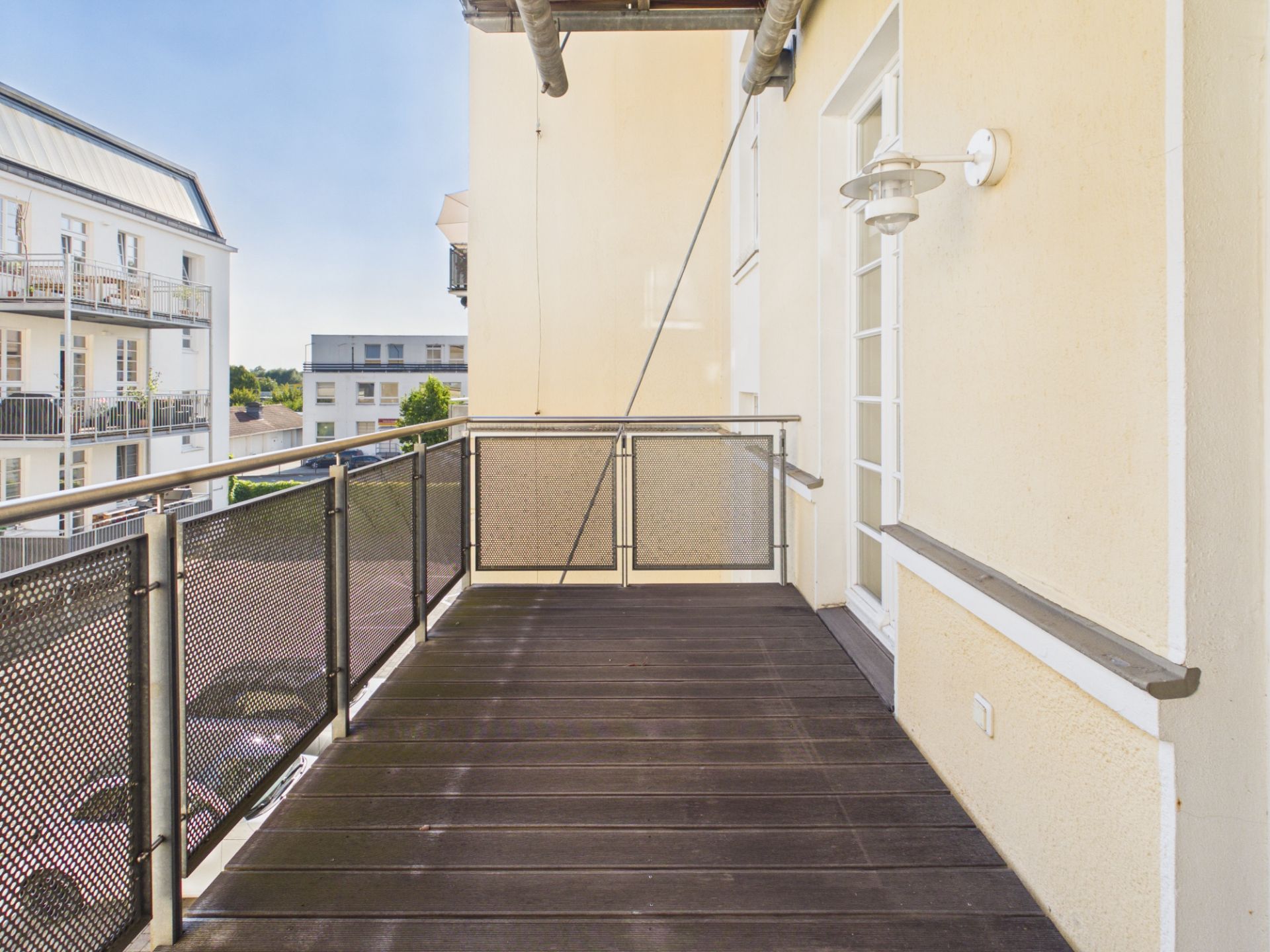 Geräumiger Balkon mit Holzboden und Metallgeländer, Blick auf Nachbargebäude.