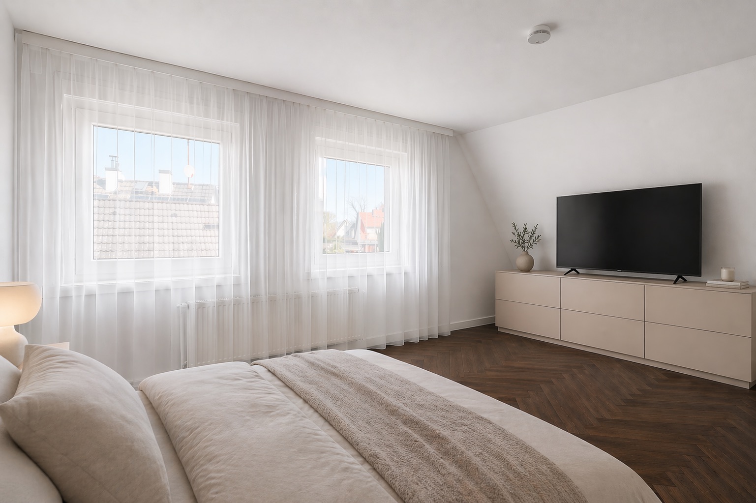 Helles Schlafzimmer mit großem Bett, zwei Fenstern, Kommode und Fernseher.