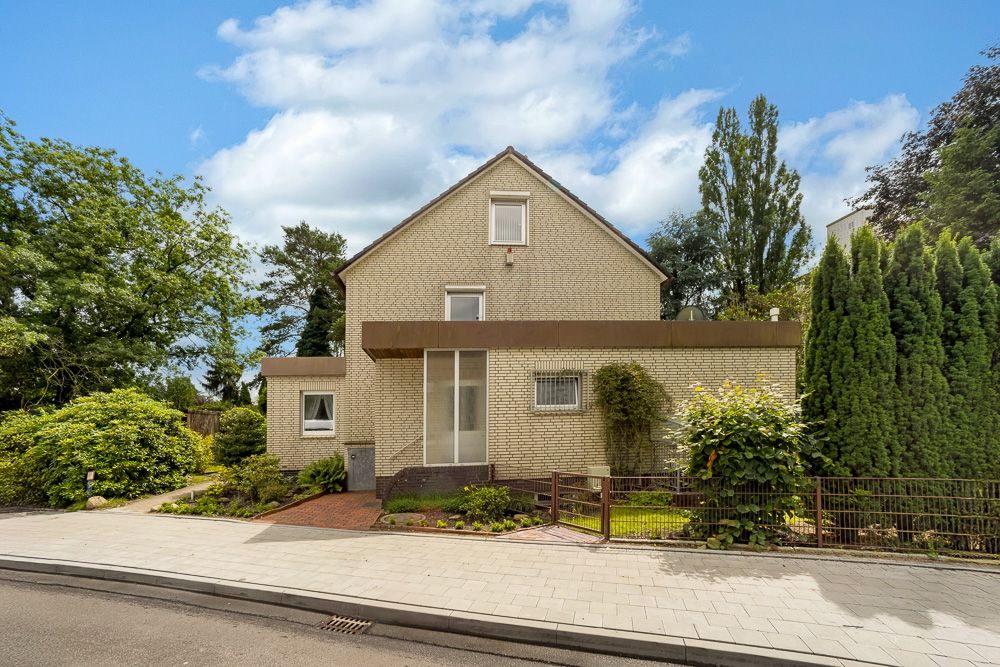 Zweistöckiges Wohnhaus mit Garten und Eingangstür, umgeben von Bäumen und Sträuchern.