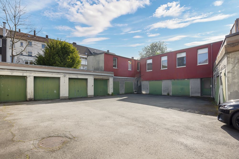 Innenhof mit mehreren grünen Garagentoren und rotem Wohngebäude im Hintergrund.