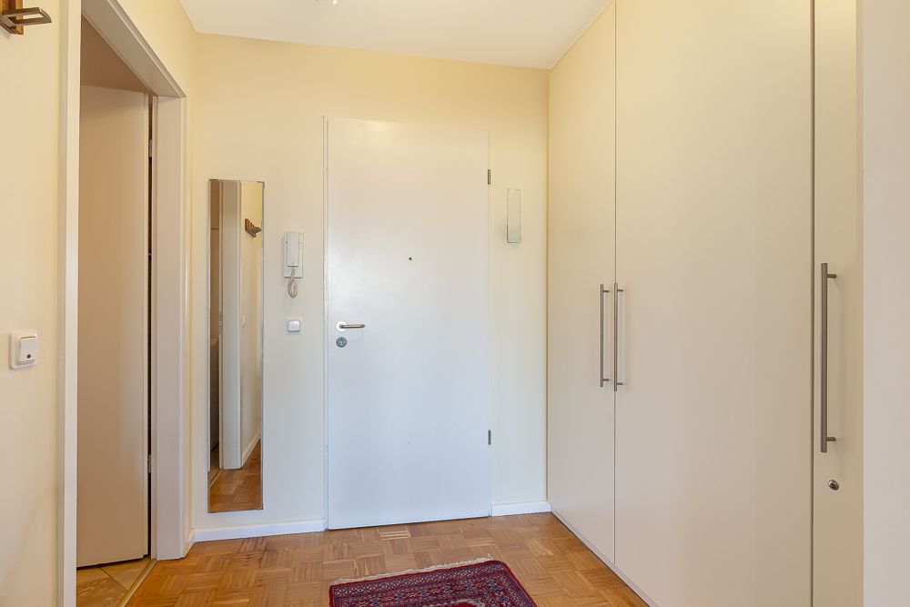 Heller Flur mit weißer Tür, großem Einbauschrank, Spiegel und kleinem Teppich.
