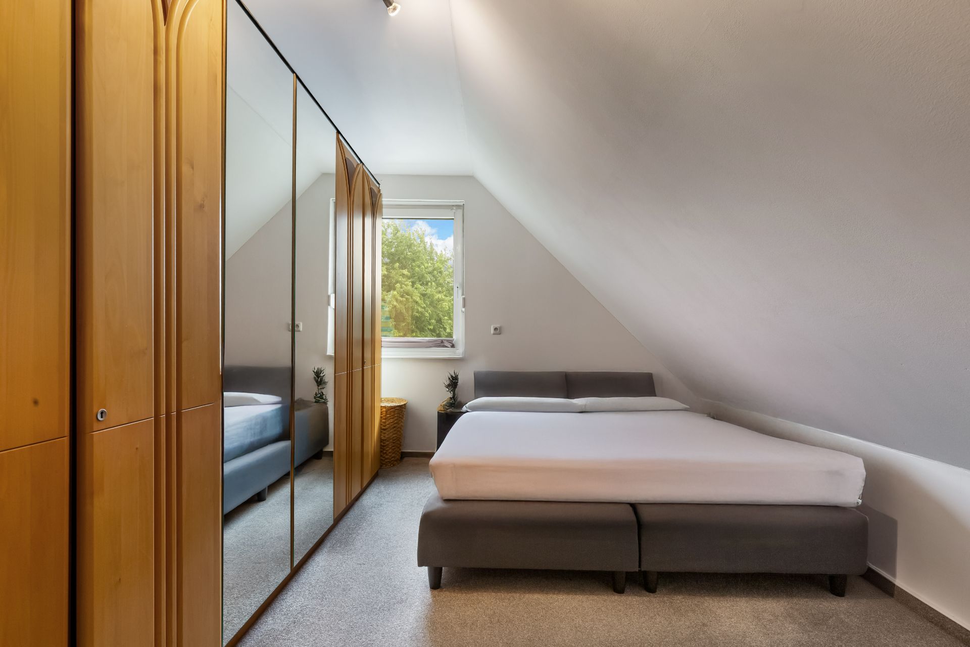 Schlafzimmer mit Doppelbett, Kleiderschrank mit Spiegel und Fenster unter einer Dachschräge.