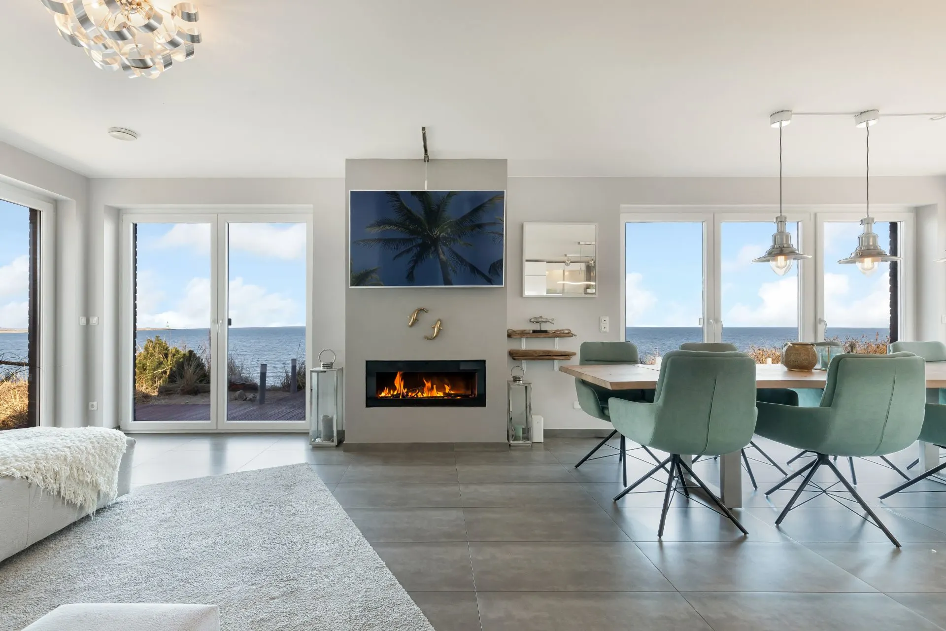 Modernes Wohnzimmer mit Kamin, Esstisch und großen Fenstern mit Meerblick.