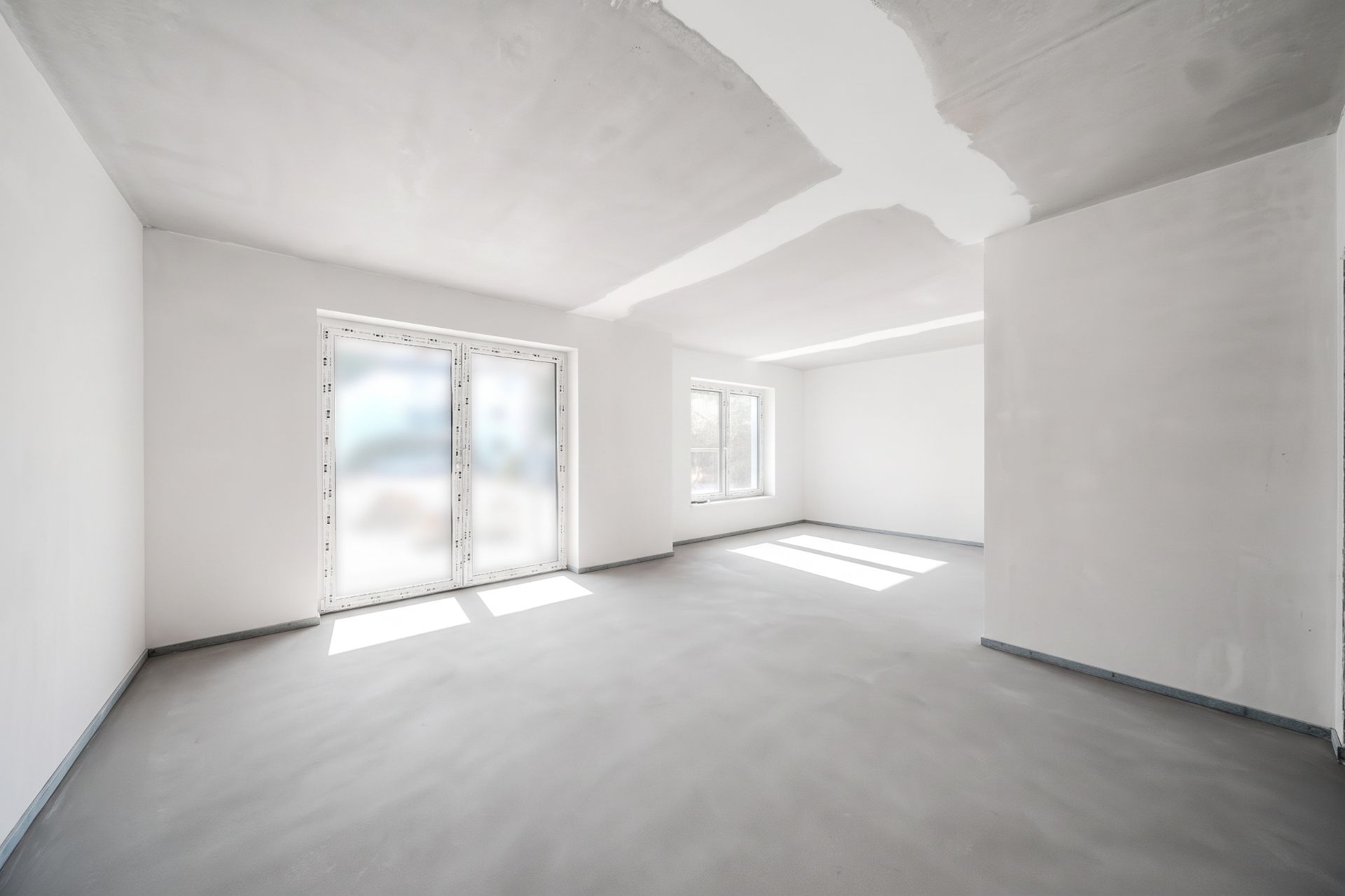 Leerer, heller Raum mit großen Fenstern und weißen Wänden in einer Wohnung.