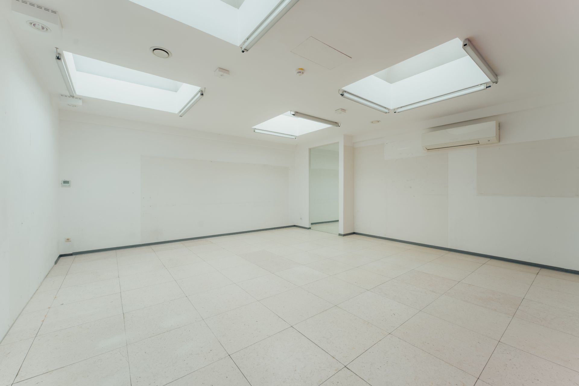 Leerer, heller Raum mit weißen Wänden, Fliesenboden und mehreren Oberlichtern in der Decke.